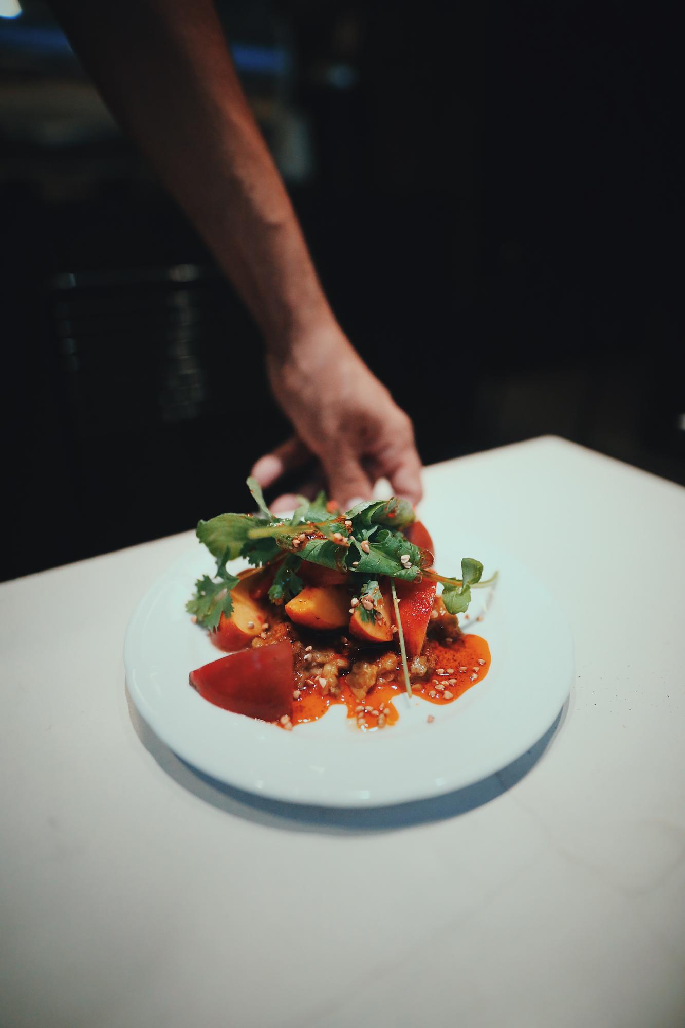 chef plating a composed dish on a dark table